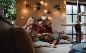 Mature father with two small children resting indoors at home, looking at photo album.